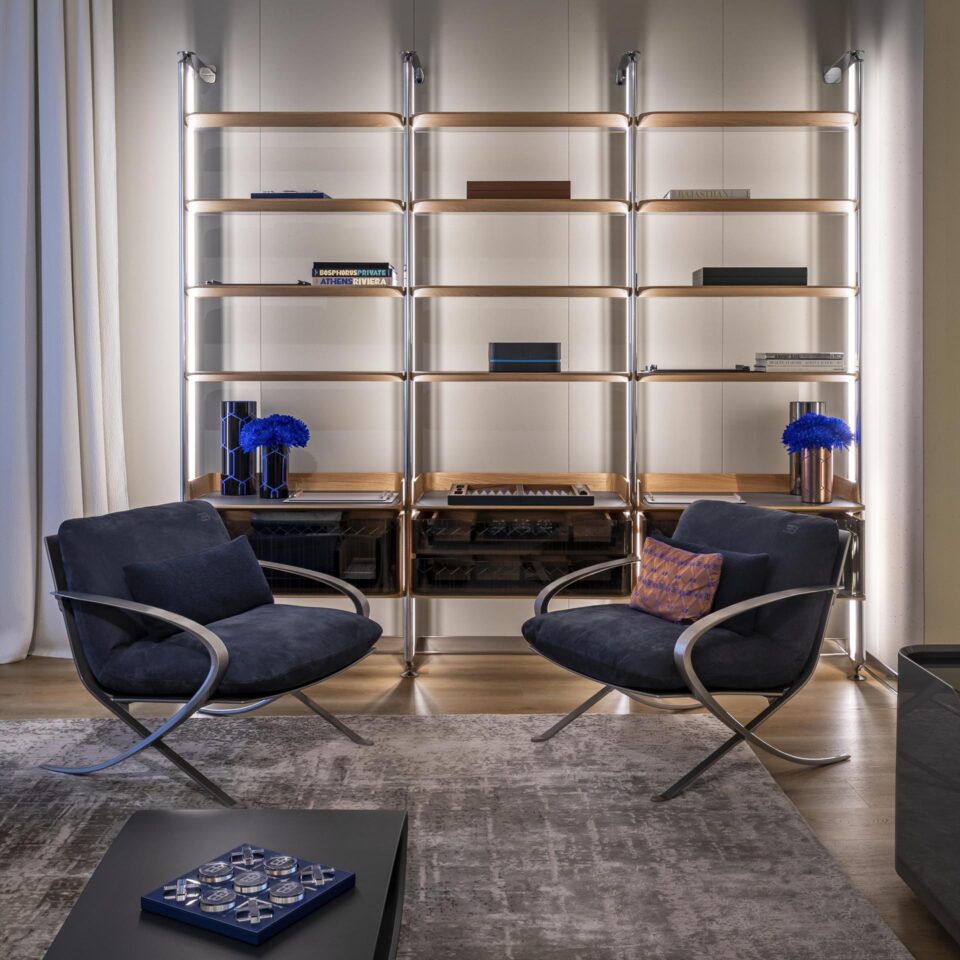 Deux fauteuils Type_17 de Bugatti Home en cuir bleu nuit, logo EB au dos du coussin, devant une bibliothèque